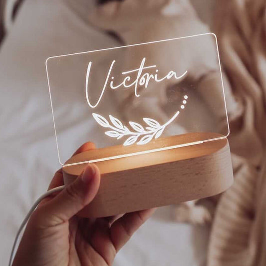 Hand holding a transparent sign with 'Victoria' and a leaf design, on a wooden base.